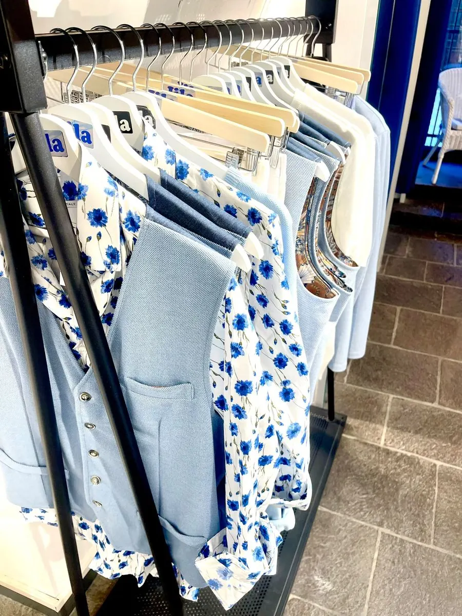 Dettaglio di camicie a fiori e polo azzurre esposte nel negozio Jila di Alassio